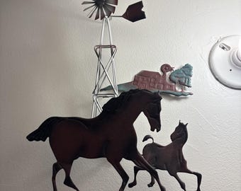 May include: Metal wall art depicting a windmill, a barn, and two horses. The windmill has a red and silver finish, while the horses and barn have a brown and green finish. Designed for wall mounting, it adds a rustic touch.