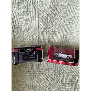 May include: Two boxed die-cast model cars. The left box is black with red accents, labeled Model Collection Scale 1:87. The right box is red and black, labeled Scale 1:72, containing a white BMW E46 M3 convertible model with a black interior.