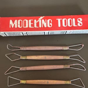 May include: A set of five clay modeling tools with wooden handles and wire loops and shapes. The tools are arranged below a red box with the words "MODELING TOOLS" in white.