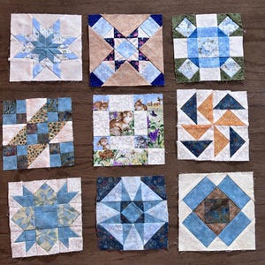 May include: Nine colorful, square quilt blocks with various geometric and floral patterns. The blocks feature shades of blue, beige, and green, with one block showcasing rabbits and flowers. The blocks are arranged on a wooden surface.