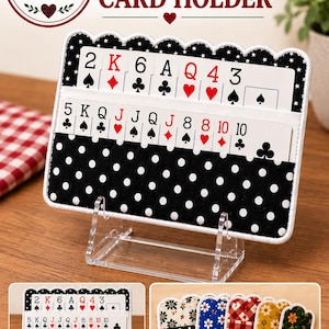 May include: A rectangular fabric playing card holder with a black and white polka dot pattern and a scalloped top edge. The holder features two horizontal slots containing various playing cards. A clear acrylic stand supports the holder.