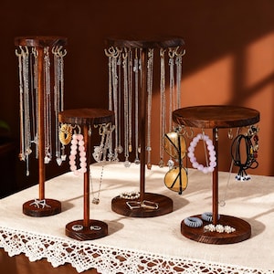 Könnte beinhalten: Vier Schmuckständer aus Holz in verschiedenen Höhen. Die Ständer haben eine dunkelbraune Oberfläche und Haken zum Aufhängen von Halsketten, Armbändern und Ohrringen. Einige Ständer halten Schmuck, darunter Halsketten, Armbänder und Ringe.