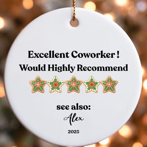 May include: A white ceramic Christmas ornament with gold string. The ornament has the text "Excellent Coworker! Would Highly Recommend" and five star-shaped cookie designs. Below the text is "see also: Alex 2025".