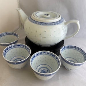 May include: A white porcelain tea set with blue geometric patterns. The set includes a teapot with a lid and four matching teacups. The teapot and cups have a delicate, pierced design.