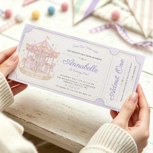 Könnte beinhalten: Eine rechteckige Einladungskarte mit hellviolettem Rand, die ein Karussell und den Text zeigt: Come One, Come All! THE GREATEST FIRST SHOW ON EARTH! Annabelle Is Turning One! SATURDAY, MAY 15TH AT 3:00 PM, ADMIT ONE.