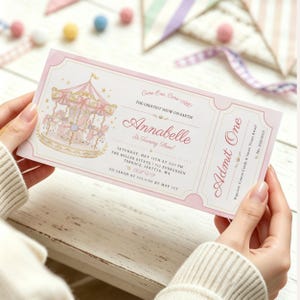 Könnte beinhalten: Eine rechteckige, rosa-weiße Geburtstagseinladung im Ticket-Design mit einer Karussell-Illustration, goldenen Sternen und dem Text Come One, Come All, The Greatest Show On Earth, Annabelle Is Turning Three, Admit One sowie Veranstaltungsdetails.