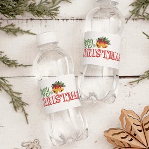 Könnte beinhalten: Zwei transparente Plastikwasserflaschen mit weißen Deckeln. Jede Flasche hat ein weißes Etikett mit den Worten "Merry Christmas" in Rot und Grün sowie einem festlichen Glocken- und Stechpalmen-Design. Auf einer weißen Holzoberfläche.