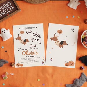 Könnte beinhalten: Zwei weiße, rechteckige Geburtstagseinladungskarten mit einem braunen Dackel, der wie eine Mumie in Bandagen gewickelt ist und einen Kürbisballon hält. Der Text lautet: A SPOOKY FIRST BOO-DAY CELEBRATION! Our Little Boo is One. Join us to celebrate Olivia's 1st Birthday.
