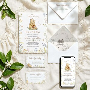 Könnte beinhalten: Ein Babyparty-Einladungsset mit einer Winnie Puuh-Illustration, bestehend aus einer Hauptkarte, zwei kleinen Karten, einem Umschlag mit Kartenfutter und einem Smartphone, das die Einladung anzeigt. Der Text lautet one little honey is on the way.