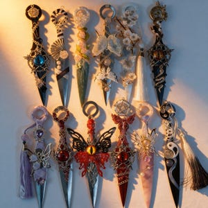 May include: Collection of decorative daggers with ornate handles and blades. Designs include butterflies, flowers, and celestial symbols. The daggers feature various colors, including black, red, and silver, with intricate detailing and embellishments.