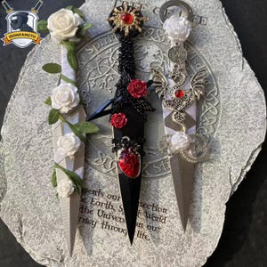 May include: Three decorative letter openers with intricate designs. One has white roses and green leaves, another features red roses and a heart pendant, and the third showcases a dragon and gears. Each has a silver blade.