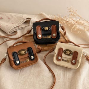 May include: Three small crossbody bags in black, brown, and cream. Each bag features a top handle, a flap with two vertical straps, silver-tone snap buttons, and a bear-shaped emblem with the text "Best" and "Bear" printed on the front.