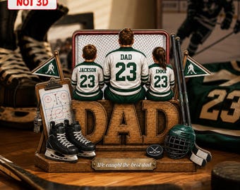 Op de afbeelding: Een houten hockey-thema decoratie met het woord "DAD". Het toont figuren in hockeytruien, een net, schaatsen, een helm en een stick. De tekst "We caught the best dad" is ook aanwezig.
