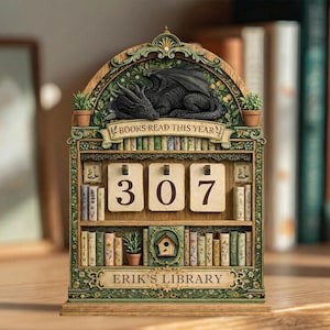 May include: Wooden bookshelf-shaped calendar with a sleeping black dragon at the top. The calendar displays the number "307" and the text "BOOKS READ THIS YEAR" and "ERIK'S LIBRARY". The design includes miniature books and potted plants.