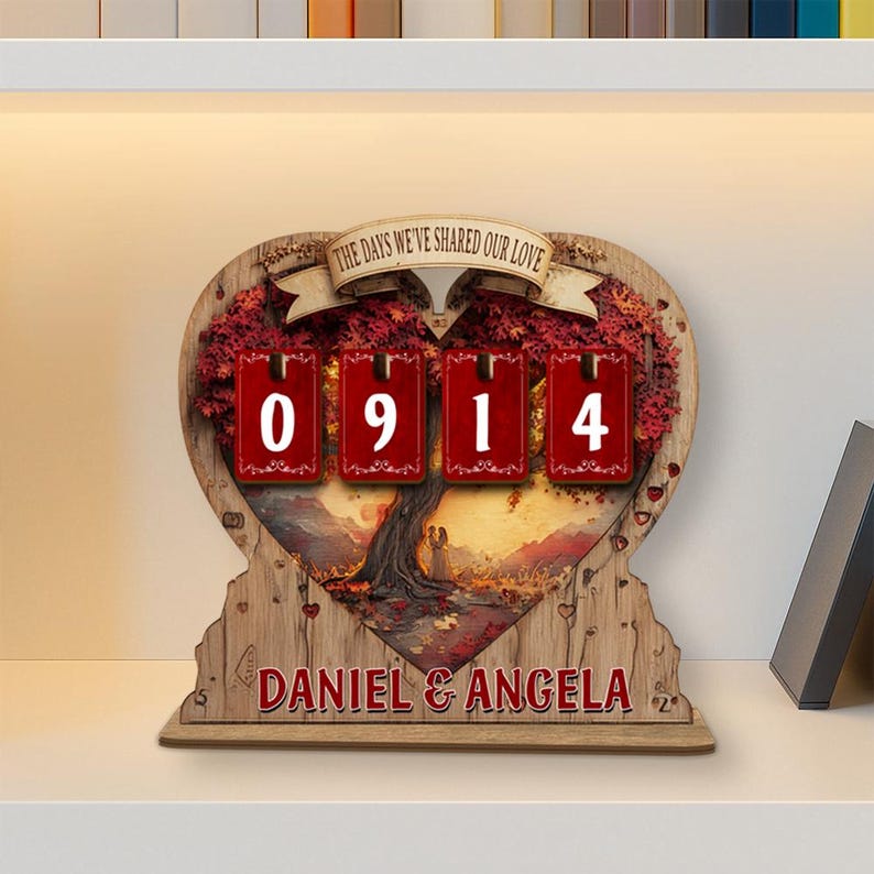 Puede incluir: Calendario de madera en forma de coraz&oacute;n con el texto "THE DAYS WE'VE SHARED OUR LOVE" y los nombres "DANIEL & ANGELA". El calendario muestra la fecha "0914" en bloques rojos. El fondo presenta un paisaje.