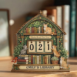 May include: A decorative wooden cat-themed library calendar with the text "Books Read This Year" and "Emily's Library." The calendar displays "021" with cat figurines, books, and greenery. The color palette includes green, brown, and orange.