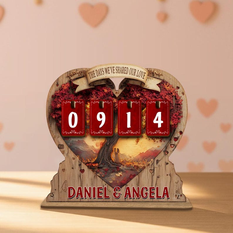 Puede incluir: Calendario de cuenta regresiva de madera en forma de coraz&oacute;n con el texto "THE DAYS WE'VE SHARED OUR LOVE". El calendario muestra el n&uacute;mero "0914" en tarjetas rojas. Los nombres "DANIEL & ANGELA" est&aacute;n impresos en la parte inferior.