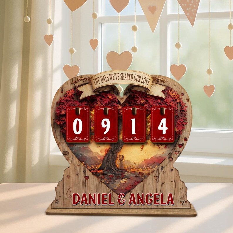 Puede incluir: Adorno de madera en forma de coraz&oacute;n con el texto "THE DAYS WE'VE SHARED OUR LOVE" y los nombres "DANIEL & ANGELA". Presenta un dise&ntilde;o de &aacute;rbol con los n&uacute;meros "0914" en tarjetas rojas. Corazones decorativos cuelgan en el fondo.
