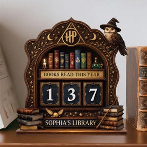 以下が含まれることがあります： 「BOOKS READ THIS YEAR」の文字と数字137が表示された、本棚スタイルの木製カレンダー。魔女の帽子をかぶった装飾的なフクロウ、本の山、そして「SOPHIA'S LIBRARY」の文字が特徴です。