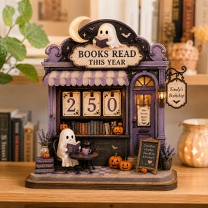 May include: A purple bookstore-themed countdown calendar featuring a ghost reading a book on the roof and another ghost sitting at a table with a black cat. The sign reads BOOKS READ THIS YEAR, with flip numbers showing 250 and a sign saying Emily's Bookshop.