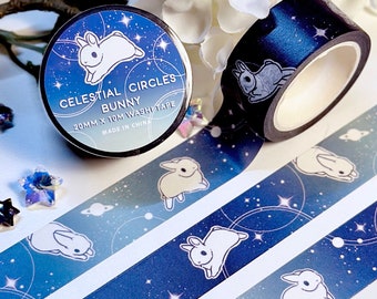 Può includere: Un rotolo di nastro washi blu e bianco con un tema celeste. Il nastro presenta coniglietti bianchi, stelle e pianeti su uno sfondo blu scuro con glitter argentato. Il nastro è largo 20 mm e lungo 10 m. L'etichetta sul rotolo recita "Celestial Circles Bunny 20mm x 10m Washi Tape Made in China."