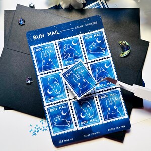 May include: A sheet of nine blue and white bunny stamp stickers with a starry night sky background. The stickers feature a bunny with a crescent moon and the text "BUN MAIL".