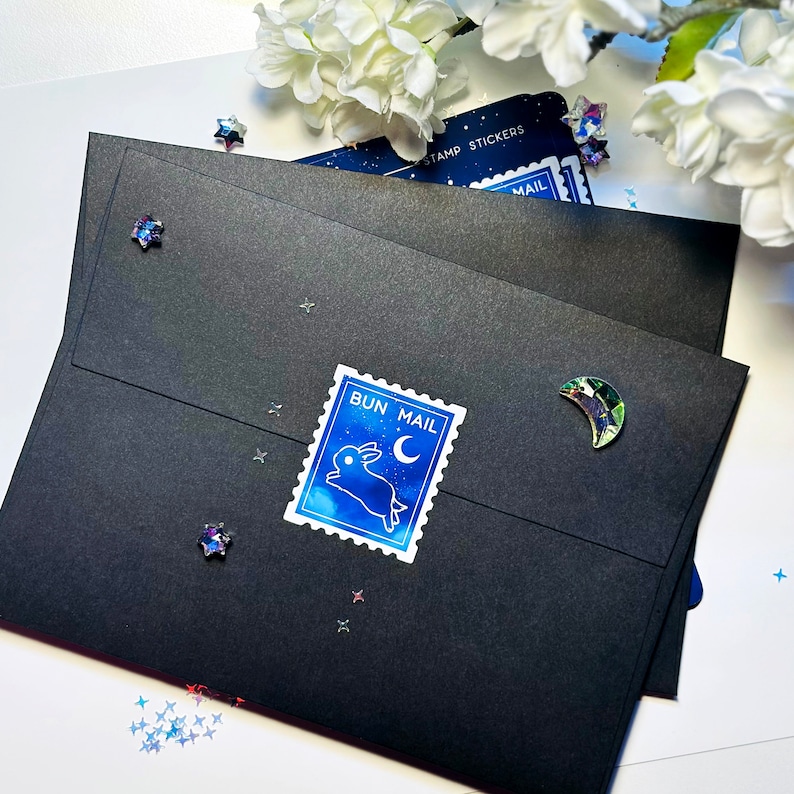May include: Three black envelopes with a blue and white bunny stamp that says "Bun Mail" on the front. The envelopes are decorated with iridescent glitter stars.