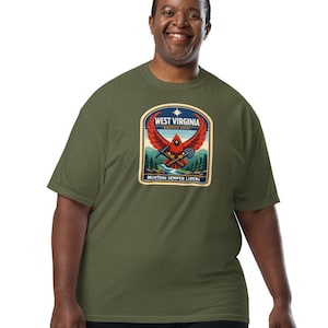 Puede incluir: Camiseta verde oliva con un emblema del estado de West Virginia. El emblema incluye un pájaro rojo, una estrella azul y las palabras "West Virginia" y "Montani Semper Liberi". La camiseta se combina con pantalones negros.
