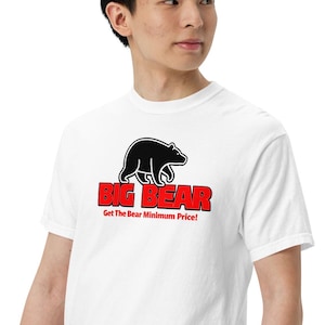 Puede incluir: Camiseta blanca con un oso negro y el texto rojo "BIG BEAR", con la frase "Get The Bear Minimum Price!". La camiseta de manga corta está hecha de un tejido suave.