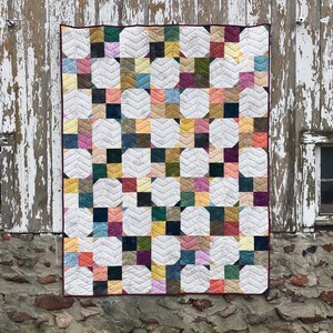 May include: A patchwork quilt with a white background and colorful squares and circles. The quilt is hanging on a wooden wall with white paint peeling off.