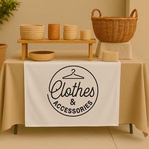 May include: A display of woven baskets and containers on a wooden shelf and table. The table runner features a black and white circular logo with the words "Clothes & Accessories". The baskets and containers are in various sizes and shades of beige and brown.
