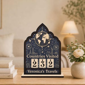 May include: A dark blue wooden sign with a pointed arch top featuring a world map, compass rose, and travel icons. The text reads Countries Visited and Veronica's Travels. Three rotating wooden blocks display the number 232 on the front surface.