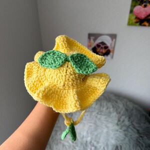 May include: A handmade yellow crochet hat with green leaf accents. The hat has a wide brim and a tie under the chin. The hat is designed to look like a lemon.