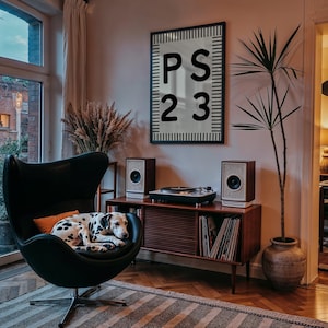 May include: A black egg chair with a Dalmatian dog resting on it. A wooden cabinet with a record player and speakers is in the background. A framed artwork with the text "PS 23" hangs on the wall.