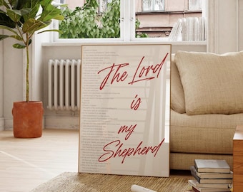 May include: A framed print with the text "The Lord is my Shepherd" in red script. The print is displayed on a light-colored wall, with a beige sofa and a potted plant in the background. The room has a neutral color palette.