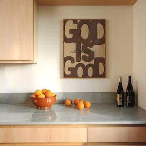 May include: A rectangular wall art print in a brown frame featuring the text GOD IS GOOD in large, bold, dark brown letters with the phrase all the time in a smaller, cursive script font centred between the larger words on a tan background.