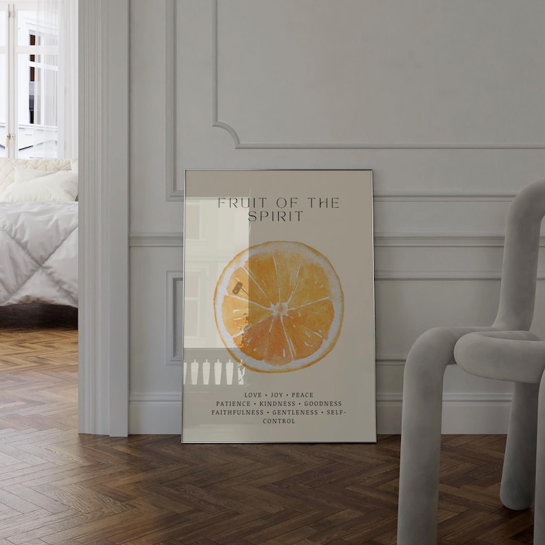 The framed “Fruit of the Spirit” orange watercolor poster stands along a bright hallway wall, with sunlight flowing from an adjacent room. The warm citrus tones and green leaf details contrast beautifully with the soft white walls. The Scripture virtues add an inspiring, faith-filled touch to the minimalist setting.