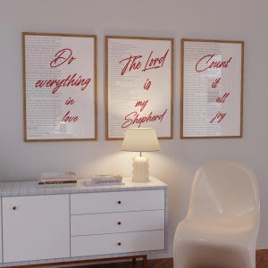 Puede incluir: Tres cuadros de pared con marcos de madera clara, cada uno con un fondo de texto pequeño en negro y letras grandes en cursiva roja. Las láminas muestran las frases Do everything in love, The Lord is my Shepherd y Count it all joy.