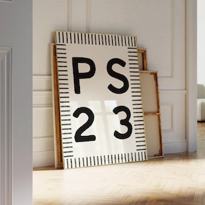 A large Psalm 23 poster with bold black “PS 23” lettering and a modern black-and-white striped border leans against an ornate white wall in a bright, elegant room. Sunlight falls across the herringbone wood floor, highlighting the framed artwork and stacked empty frames around it for a warm, serene aesthetic.