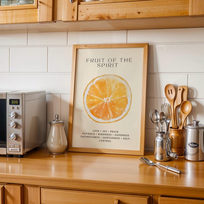 Christian wall art print with watercolor orange design leaning on a kitchen counter. Surrounded by utensils and soft light, the portrait composition blends faith and everyday warmth.