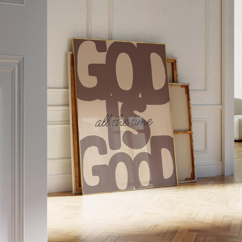 May include: A rectangular wall art print in a thin gold frame featuring the text GOD IS GOOD in large, bold, dark brown block letters against a light beige background, with the phrase all the time written in a smaller, dark brown cursive script.