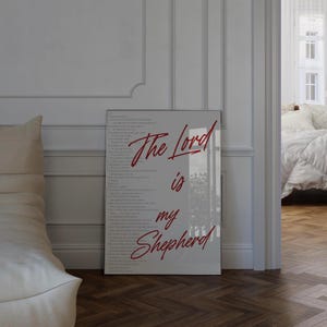 May include: A framed print with the words "The Lord is my Shepherd" in red script. The print has a white background with the full text of Psalm 23 in a light gray font. The frame is a light gray color.