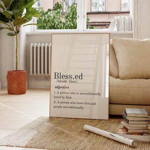 Puede incluir: Un cuadro enmarcado con la palabra "Blessed" y su definición. El cuadro está en un marco dorado y se exhibe en un salón. La definición incluye dos puntos sobre ser amado por Dios y amar a los demás.