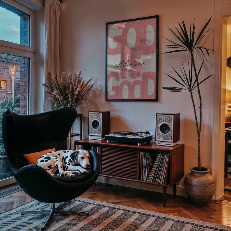 May include: Interior shot featuring a black egg chair with a Dalmatian dog resting on it. A wooden cabinet holds a record player and speakers. A framed poster with the words "GOD IS GOOD" hangs on the wall. A potted plant is in the corner.