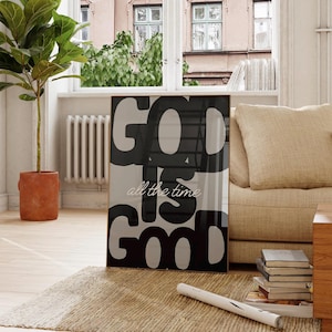 Könnte beinhalten: Ein gerahmter Kunstdruck mit den Worten "GOD IS GOOD all the time" in Schwarz und Weiß. Das Kunstwerk wird auf einem Teppich vor einem Fenster mit einem Sofa und einer Topfpflanze im Hintergrund ausgestellt. Der Druck hat einen goldenen Rahmen.