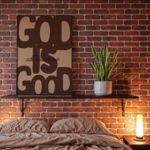 May include: A rectangular wall art print featuring the dark brown text GOD IS GOOD in a bold, rounded font against a light brown background, with the phrase all the time written in a smaller, cursive black script centred between the words.