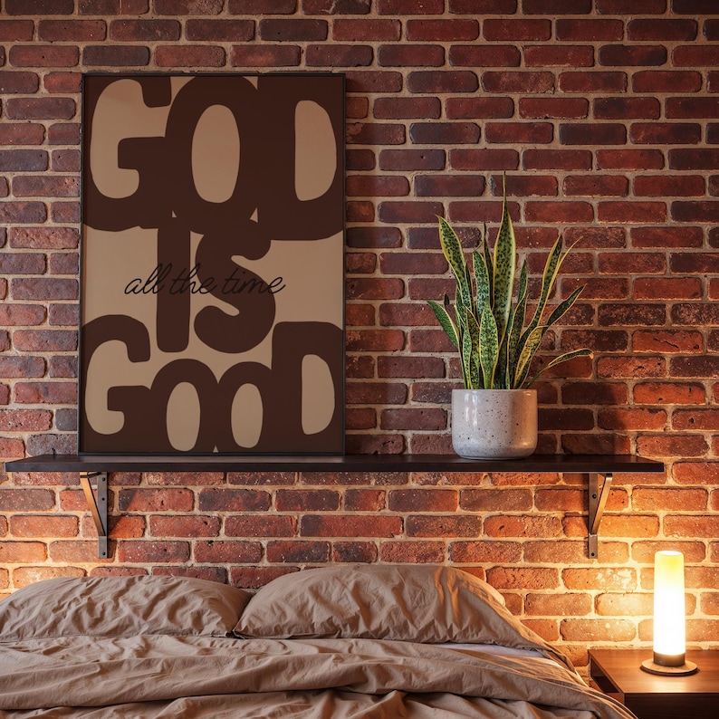May include: A rectangular wall art print featuring the dark brown text GOD IS GOOD in a bold, rounded font against a light brown background, with the phrase all the time written in a smaller, cursive black script centred between the words.