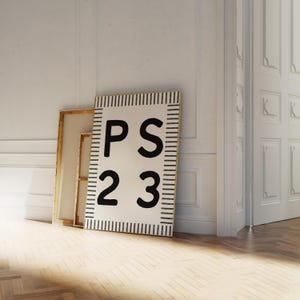 May include: A rectangular canvas print with the text "PS 23" in bold black letters. The print has a white background with black vertical lines along the edges, resembling a ruler. The print is leaning against a wall next to another framed canvas.