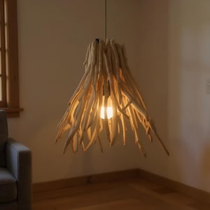 May include: A unique pendant light fixture crafted from natural driftwood. The light fixture has a conical shape, with numerous light-colored wooden branches radiating outwards. A single light bulb is visible at the center, casting a warm glow. The fixture hangs from a black cord.