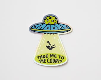 Peut inclure: Un autocollant représentant une soucoupe volante de dessin animé bleue et jaune, projetant un rayon sur un joueur de tennis. Le texte "TAKE ME TO THE COURTS" est en vert et jaune. L'autocollant a une finition holographique.